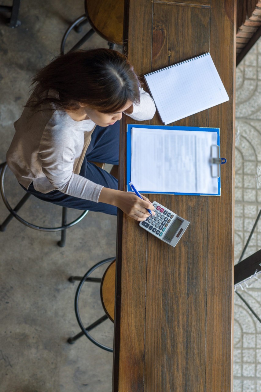 asian woman sitting at desk using calculator and completing a form